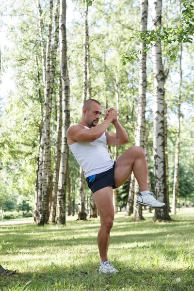 Genç bir atletik adam bir yaz günü parkta huş ağaçlarının arasında tekme atıyor..