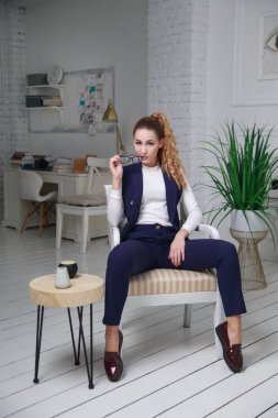 Ofisin içindeki sevimli bir kız gündelik giysiler içinde bir sandalyede oturuyor..