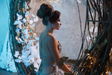 Yüksek saç stiline sahip bir kadının portresi kar kraliçesi suretinde gizemli bir mavi ışıkta, arkadan manzaralı bir peri masalı..