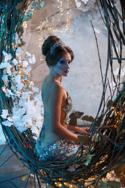 Yüksek saç stiline sahip bir kadının portresi kar kraliçesi suretinde gizemli bir mavi ışıkta, arkadan manzaralı bir peri masalı..