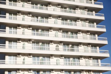 Güneşli bir günde balkonları ve pencereleri gökyüzüne bakan beyaz bir binanın ön cephesinin bir parçası..