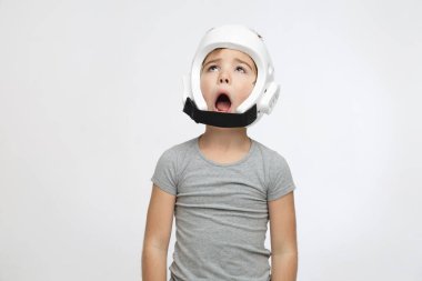 Koruyucu kasklı, acı çeken küçük bir çocuk açık gri bir arka planda izole edilmiş görünüyor..