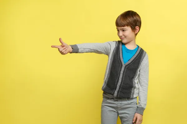 穿着休闲装的可爱的笑脸男孩举起大拇指指向左边 与黄色背景隔离 — 图库照片