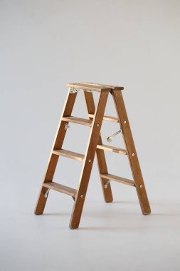 Açık gri arkaplanda basamakları olan yüksek katlanmış ahşap tabure.