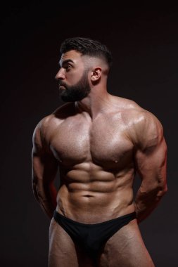 Sakallı genç atletik erkek sporcu koyu bir arka planda izole olmuş kaslar gösteriyor..
