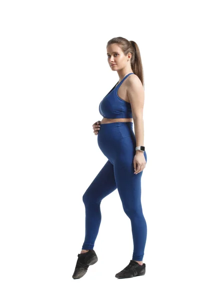 かわいいですエレガントな妊娠中の女性で青スポーツウェアスタンドで完全な成長で白い背景に隔離 — ストック写真