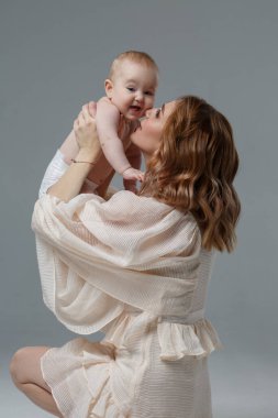 Anne kollarında tatlı bir bebek tutuyor. Gri bir arka planda izole edilmiş..