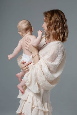 Anne kollarında tatlı bir bebek tutuyor. Gri bir arka planda izole edilmiş..