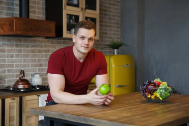 Mutfağın içinde elinde elma olan genç ve çekici bir adam..