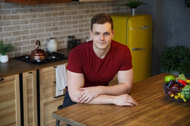 Genç ve çekici bir adam sıcak bir mutfağın içinde oturuyor..