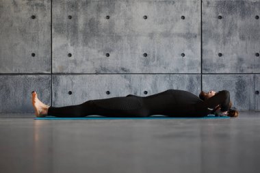 Siyah rahat spor giyimli genç sakallı bir adam içeride yoga yapıyor..