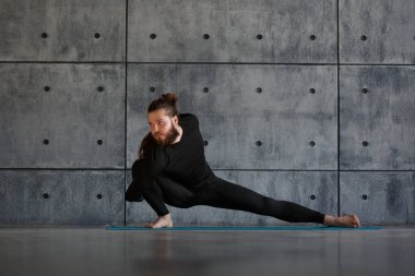 Sakallı genç bir adam spor salonunda yoga yapıyor..