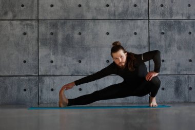Sakallı genç bir adam spor salonunda yoga yapıyor..