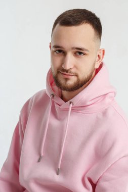 Açık gri bir arka planda izole edilmiş pembe kazaklı yakışıklı bir genç adam portresi..