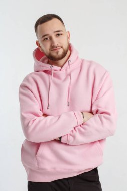 Açık gri bir arka planda izole edilmiş pembe kazaklı yakışıklı bir genç adam portresi..