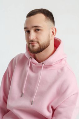 Açık gri bir arka planda izole edilmiş pembe kazaklı yakışıklı bir genç adam portresi..