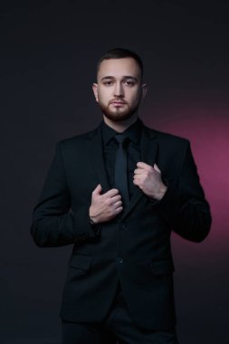 Young handsome man with a beard in a black classic suit on a dark background.