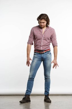 A nice guy with long hair in jeans stands in the studio in full growth.