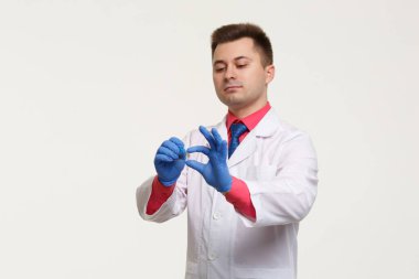 A male laboratory assistant in a white coat and gloves holds a slide and a test isolated on a light gray background.