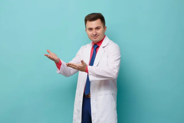 Young Smiling Male Doctor White Coat Points Two Hands Side — Stock Fotó