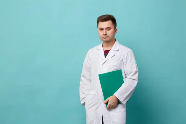 Young Handsome Doctor White Coat Holding Green Folder Isolated Blue — Stock Photo, Image