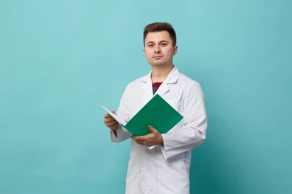 Young Handsome Doctor White Coat Holding Green Folder Isolated Blue — Stock fotografie