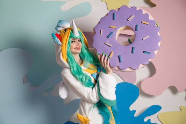 Elinde kocaman bir çörekle tek boynuzlu at gibi giyinmiş bir kız..