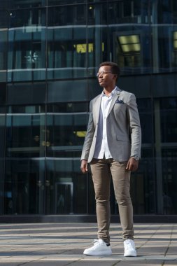 Takım elbiseli çekici bir siyahi, şehrin arka planında tam gelişim gösteriyor..