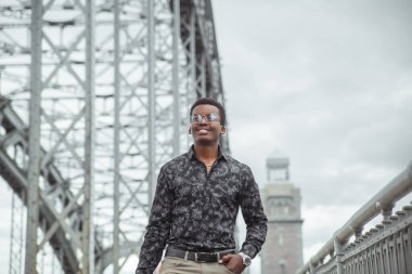 Genç gülümseyen çekici siyah adam köprüde yürüyor..