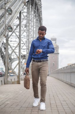 Sıradan giysiler içinde genç bir siyah adam elinde bir iş çantasıyla köprüden geçiyor..