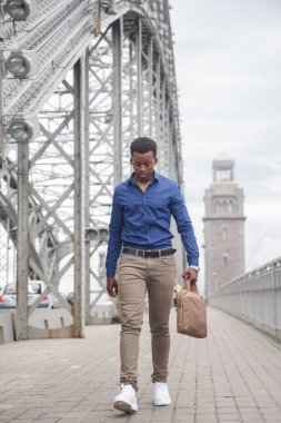 Sıradan giysiler içinde genç bir siyah adam elinde bir iş çantasıyla köprüden geçiyor..