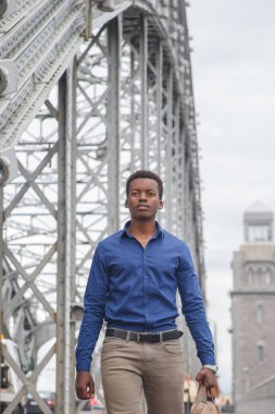 Sıradan giysiler içinde genç bir siyah adam elinde bir iş çantasıyla köprüden geçiyor..