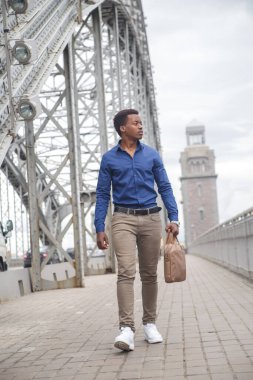 Sıradan giysiler içinde genç bir siyah adam elinde bir iş çantasıyla köprüden geçiyor..