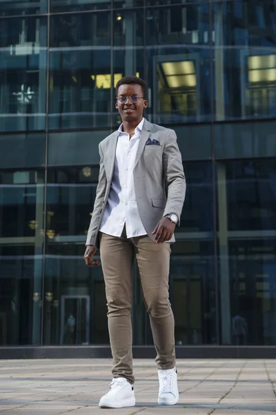 Young attractive black man in a business suit smiles and walks against the backdrop of an office building.
