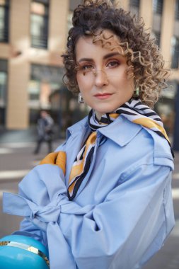 Şehirde rüzgarlı bir havada mavi yağmurluklu, kıvırcık saçlı, zarif kadınlar..