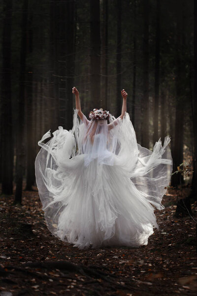 The girl the bride in a long white dress and a veil is dancing in a gloomy forest.