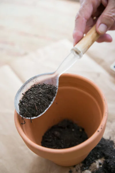 Human hand with a big spoon adding soil to a clay pot. Directly above. Vertical shot