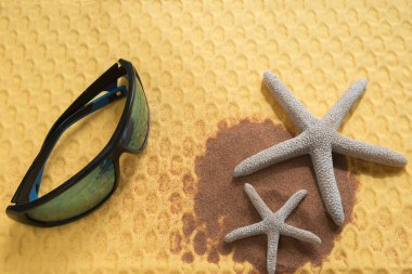 Yaz konsepti, güneş gözlüklü, deniz yıldızı ve kumsal kumsalında canlı sarı arka planda düz uzanmak.