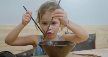 Küçük sevimli sarışın kız Doğu lokantasında çubuklarla yemek yiyor..