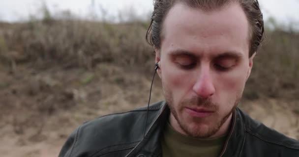 Young man in a leather jacket enjoys food and music with headphones on a picnic — Vídeo de Stock