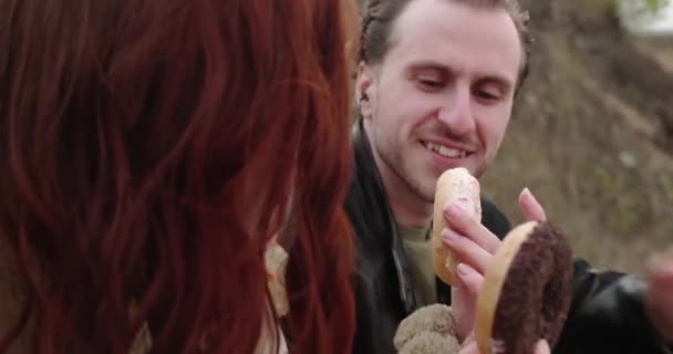 Happy couple enjoys eating doughnuts sitting at picnic — Vídeo de Stock
