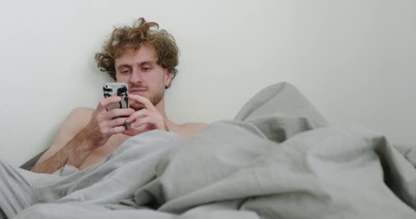 Jongeman ontspannen in de slaapkamer na het wakker worden in de ochtend — Stockvideo
