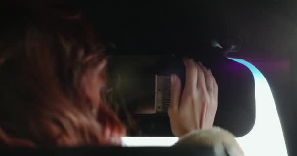 Jonge roodharige vrouw kijkt naar de camera door de spiegel in de auto — Stockvideo