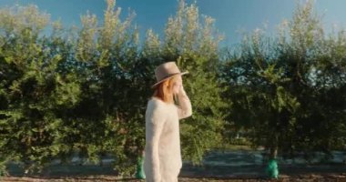 Şık bir kadın güneşli bir günde zeytin ağaçları arasında yürüyor.