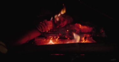 Yanmış odunları şömineye sopayla itiyor.