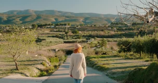 Back view of woman with hat walking along the road on background the mountains — Vídeo de Stock