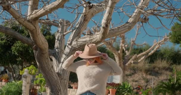 Woman tourist with hat stands near big bare tree posing for photo — Vídeo de Stock