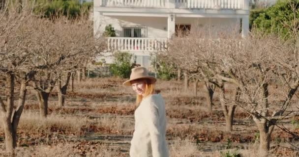 Mulher caminha entre árvores nuas em direção a grande casa de dois andares — Vídeo de Stock