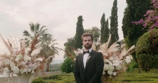 Fiatal vőlegény áll közelében luxus virágcsokrok az esküvőn — Stock videók