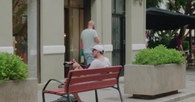 Genç müzisyen şehirde tahta bankta gitar çalıyor.